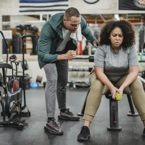 Personal male trainer with overweight female client in fitness center