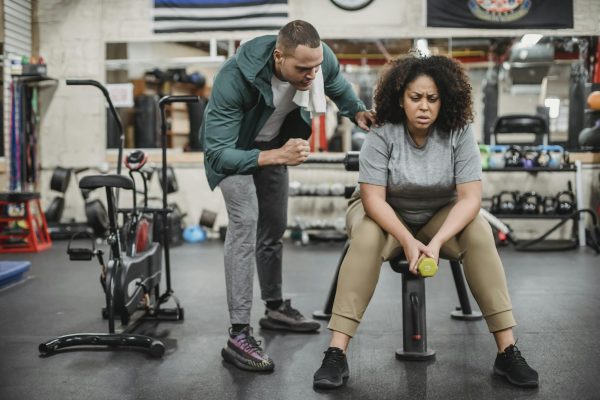 Personal male trainer with overweight female client in fitness center